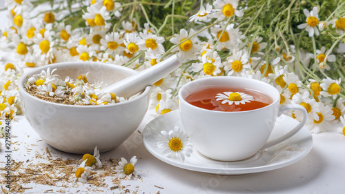 Rural still-life - cup of brewed chamomile tea on the background of a bouquet of daisies, closeup