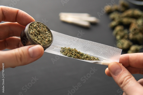 Cannabis buds on black table, rolled joint with weed, close up, grinder in hand with fresh marijuana, photo