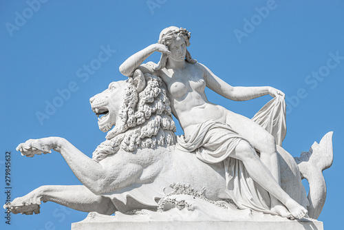 Old statue of sensual renaissance era woman laying on big lion at blue smooth background, Potsdam, Germany, details, closeup
