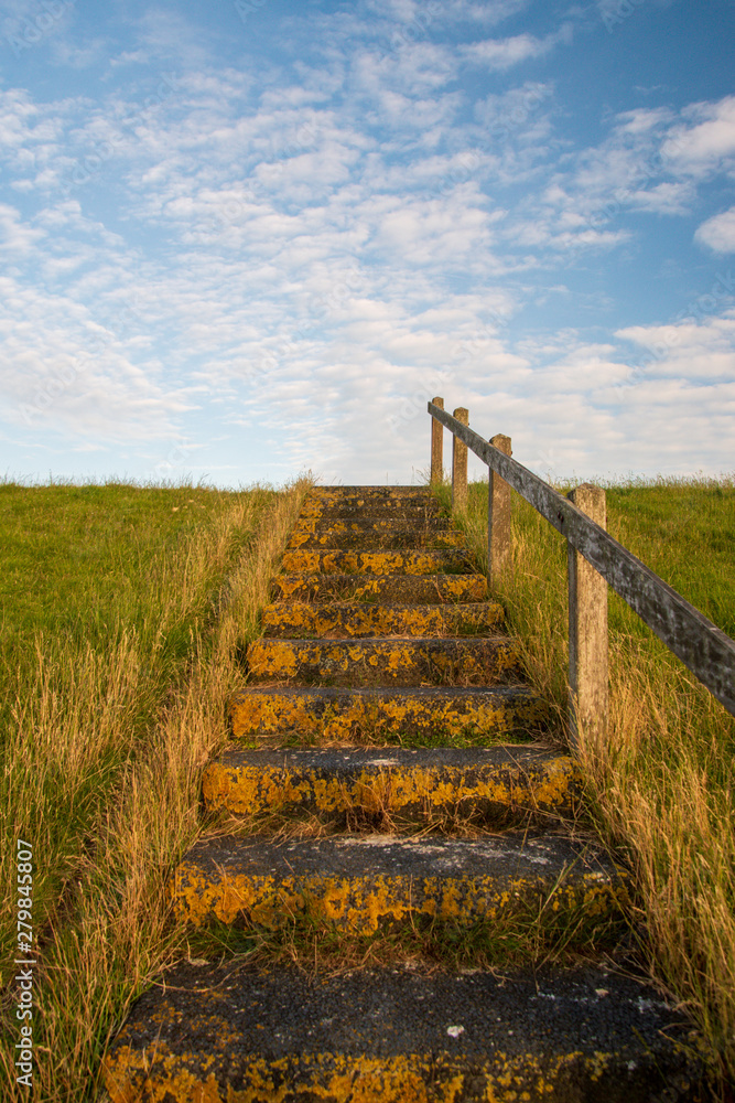 Stairway on a dike under a blue sky with cumulus clouds.