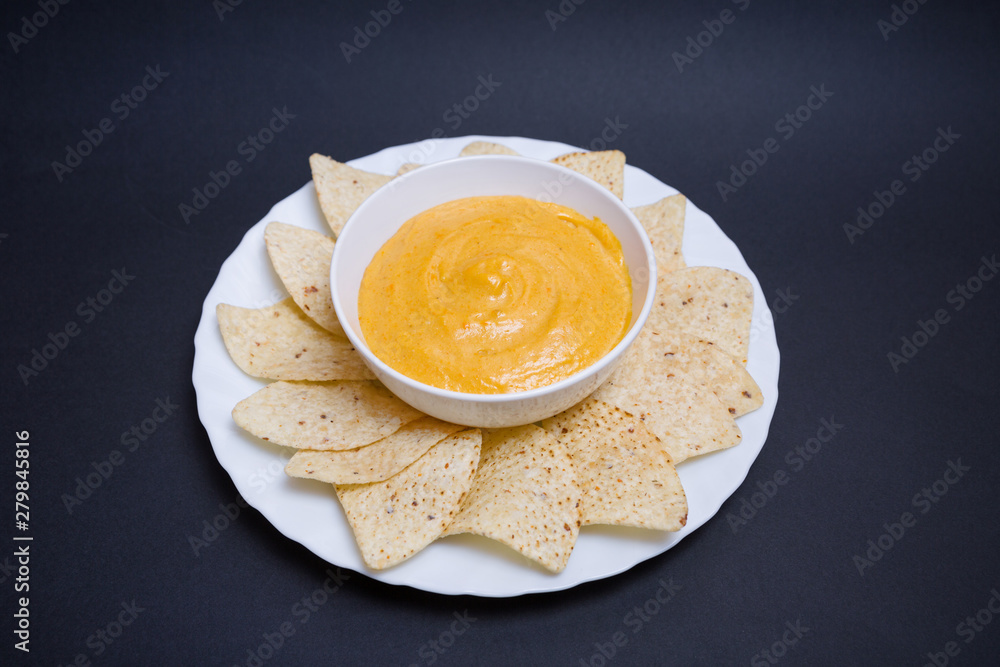 Queso chedar vegano con nachos para mojar sobre fondo negro. Queso chedar vegano con nachos para mojar sobre fondo negro.