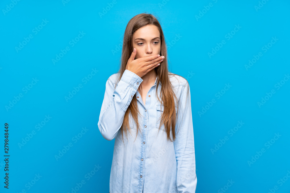 Young woman over isolated blue background covering mouth with hands Young woman over isolated blue background covering mouth with hands