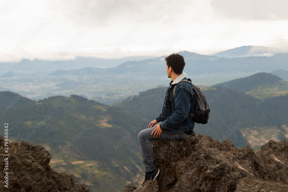 Naklejka premium Latin man sitting on top of a cliff with the mountains behind him