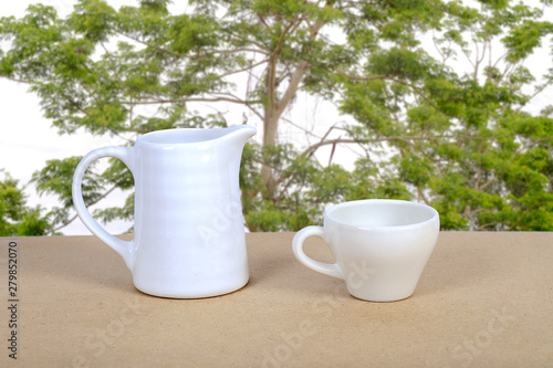 White coffee cup and jar on wood table with nature background.