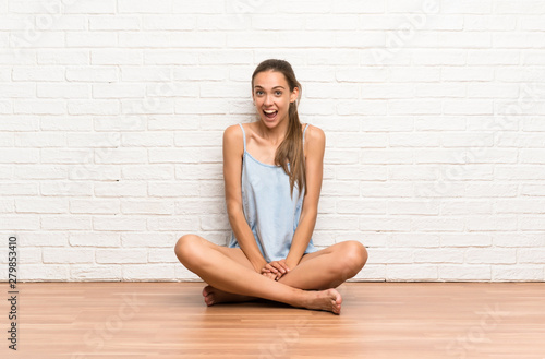 Young woman sitting on the floor with surprise facial expression