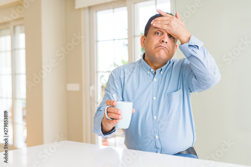 Middle age man drinking coffee in the morning at home stressed with hand on head, shocked with shame and surprise face, angry and frustrated. Fear and upset for mistake.