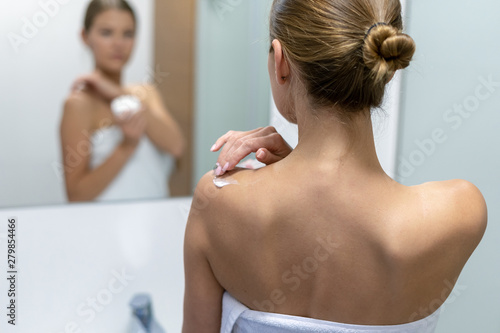 Woman applying body cream on shoulder in bathroom