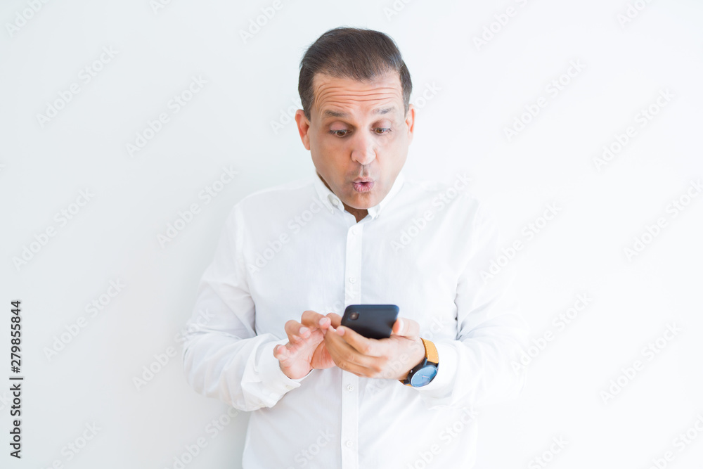 Middle age man using smartphone over white wall scared in shock with a surprise face, afraid and excited with fear expression Middle age man using smartphone over white wall scared in shock with a surprise face, afraid and excited with fear expression