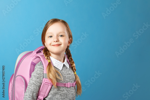 Portrait of a little girl schoolgirl with a backpack on a blue background. Back to school. The concept of education. Copy space.