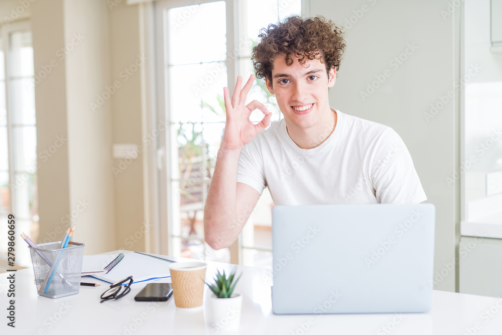 Young student man working and studying using computer laptop doing ok sign with fingers, excellent symbol Young student man working and studying using computer laptop doing ok sign with fingers, excellent symbol