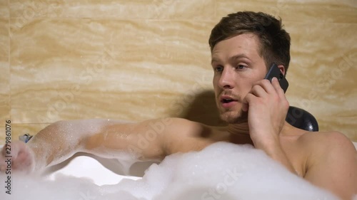 Anger man quarrelling with girlfriend on mobilephone, taking relaxing foambath photo
