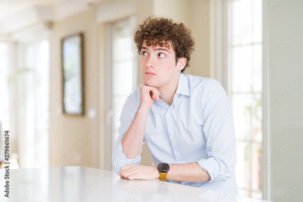 Young business man with curly read head with hand on chin thinking about question, pensive expression. Smiling with thoughtful face. Doubt concept.