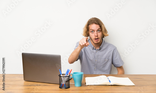 Blonde man with a laptop surprised and pointing front © luismolinero