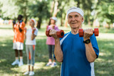 selective focus of happy senior man holding dumbbells in park