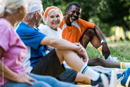 selective focus of happy multicultural men and women in sportswear sitting on fitness mats