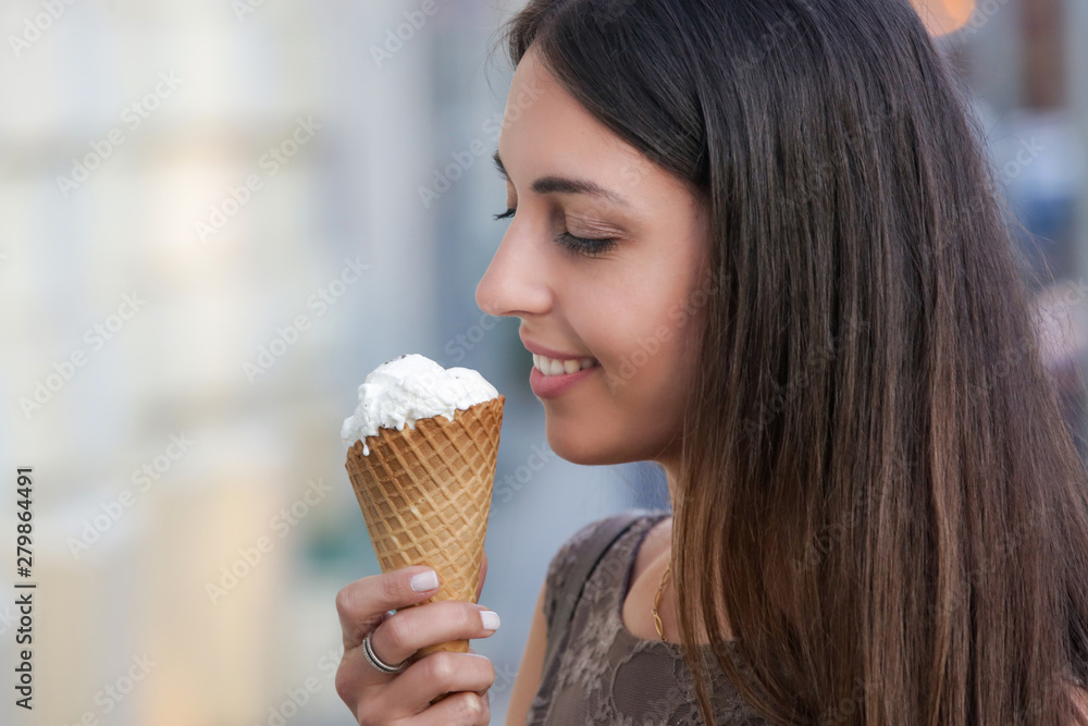 The young smiling woman in the city street holding vanilla ice cream cone The young smiling woman in the city street holding vanilla ice cream cone