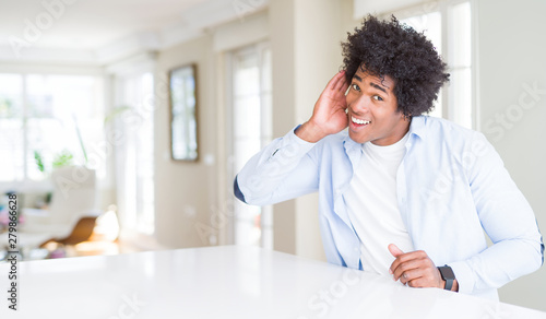 African American man at home smiling with hand over ear listening an hearing to rumor or gossip. Deafness concept.