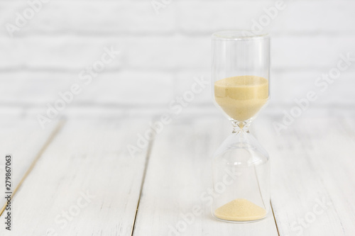 Hourglass on white wood table over white brick background with copy space.