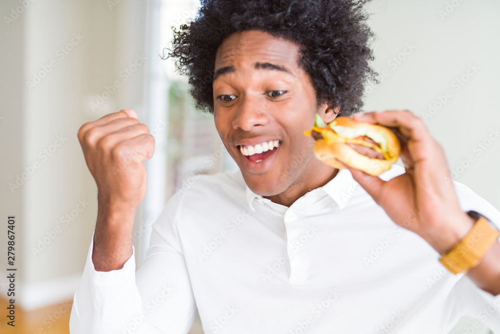 African American hungry man eating hamburger for lunch screaming proud and celebrating victory and success very excited, cheering emotion African American hungry man eating hamburger for lunch screaming proud and celebrating victory and success very excited, cheering emotion