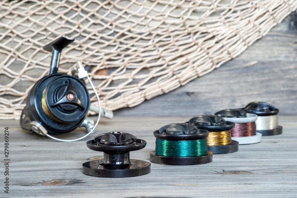 Set with multi-colored spools with fishing line for fishing on the  background of spinning reels on wooden background. Stock Photo