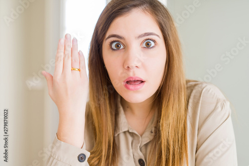 Beautiful young woman showing alliance ring on hand scared in shock with a surprise face, afraid and excited with fear expression