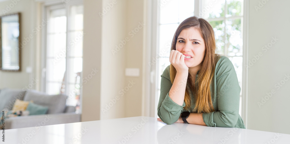 Beautiful young woman at home looking stressed and nervous with hands on mouth biting nails. Anxiety problem.