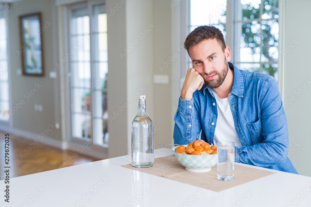 Handsome man eating pasta with meatballs and tomato sauce at home thinking looking tired and bored with depression problems with crossed arms. Handsome man eating pasta with meatballs and tomato sauce at home thinking looking tired and bored with depression problems with crossed arms.