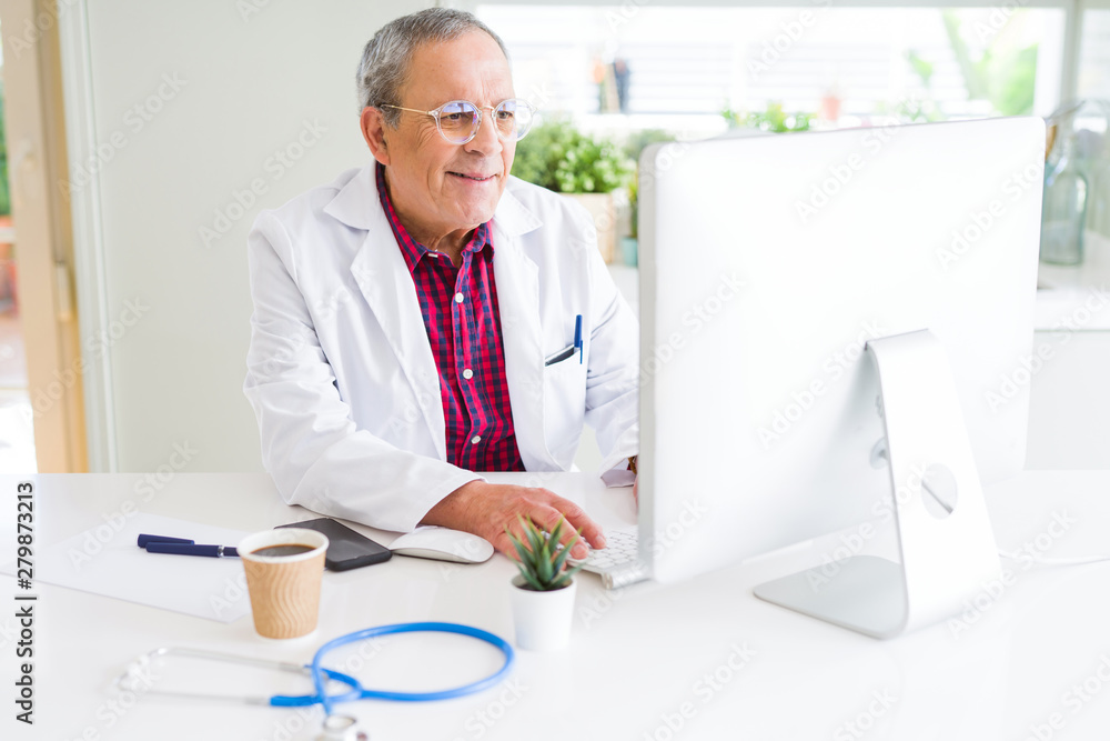 Obraz premium Senior doctor man at the clinic working with computer and smiling