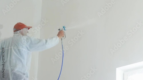 repair of the apartment - professional painter paints the walls with white paint spray gun