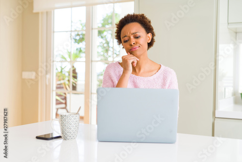 Young african american woman working using computer laptop with hand on chin thinking about question  pensive expression. Smiling with thoughtful face. Doubt concept.