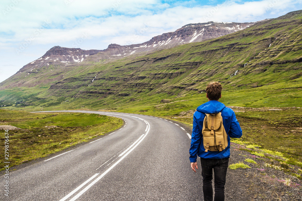 Hiker walking on the road in Iceland surrounded by beautiful mountains and waterfalls. Travel / vacation concept. Outdoor shot.