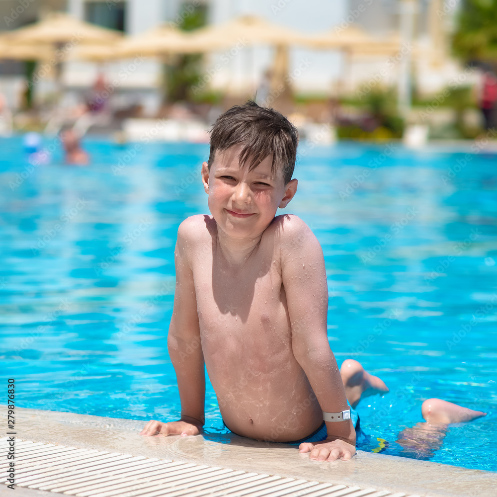 Happy smiling boy on side of swimming pool. He is looking at camera.