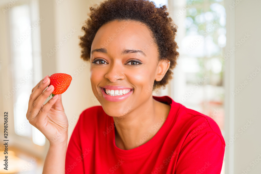 Young african american woman eating fresh strawberries for breakfast with a happy face standing and smiling with a confident smile showing teeth Young african american woman eating fresh strawberries for breakfast with a happy face standing and smiling with a confident smile showing teeth