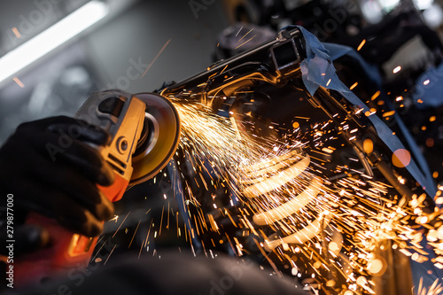 Worker cutting, grinding and polishing motorcycle metal part with sparks indoor workshop, close-up.
