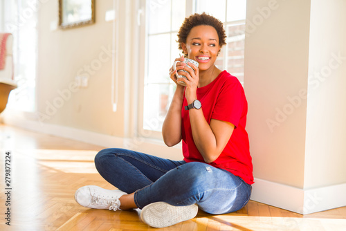 Beautiful young african american woman sitting on the floor at home and drinking a cup of coffee