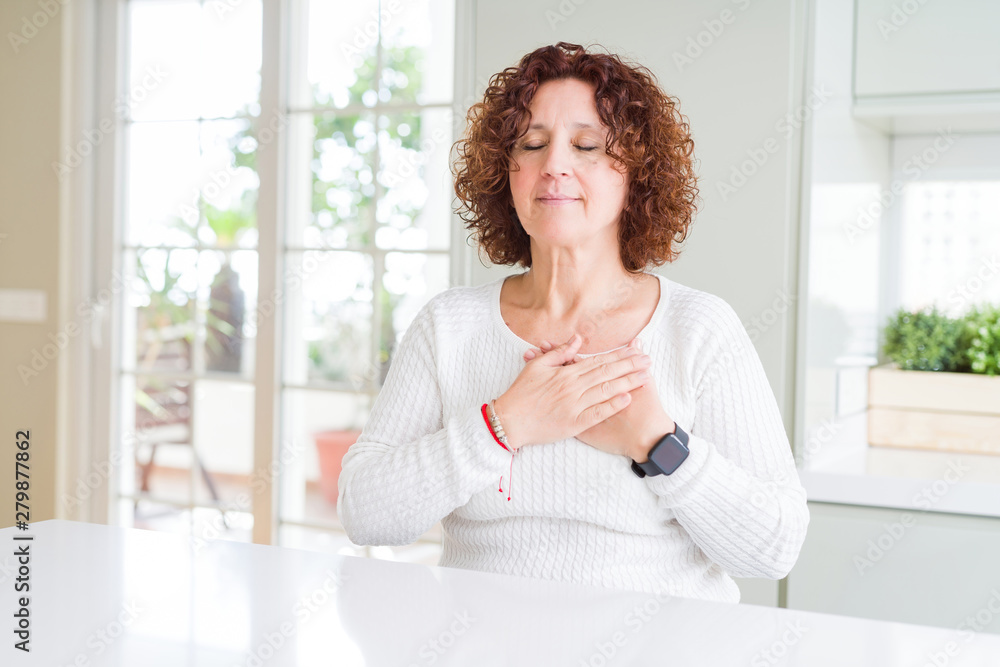 Beautiful senior woman wearing white sweater at home smiling with hands on chest with closed eyes and grateful gesture on face. Health concept. Beautiful senior woman wearing white sweater at home smiling with hands on chest with closed eyes and grateful gesture on face. Health concept.