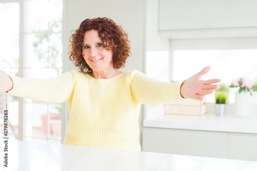 Beautiful senior woman wearing yellow sweater looking at the camera smiling with open arms for hug. Cheerful expression embracing happiness.