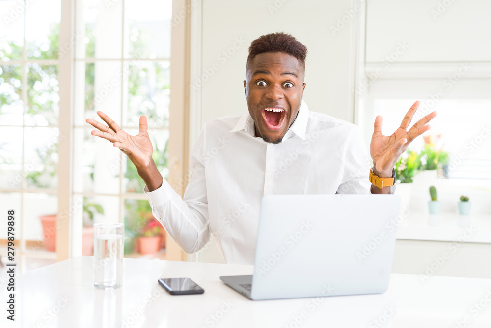 African american business man working using laptop celebrating crazy and amazed for success with arms raised and open eyes screaming excited. Winner concept