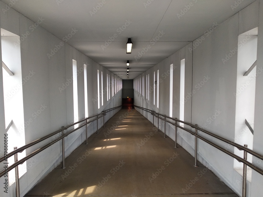 white, well-lit tunnel with handrails. the road is inclined to descend down, under the ground or on the floor below. ease of use even for people with disabilities.