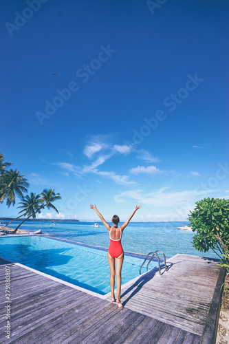 Feel freedom! Young woman in red swimsuit enjoying the view near swimming pool on tropical beach.