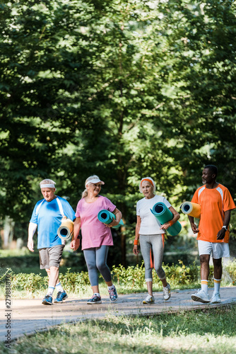 selective focus of senior and multicultural pensioners holding fitness mats and walking in walkway © LIGHTFIELD STUDIOS
