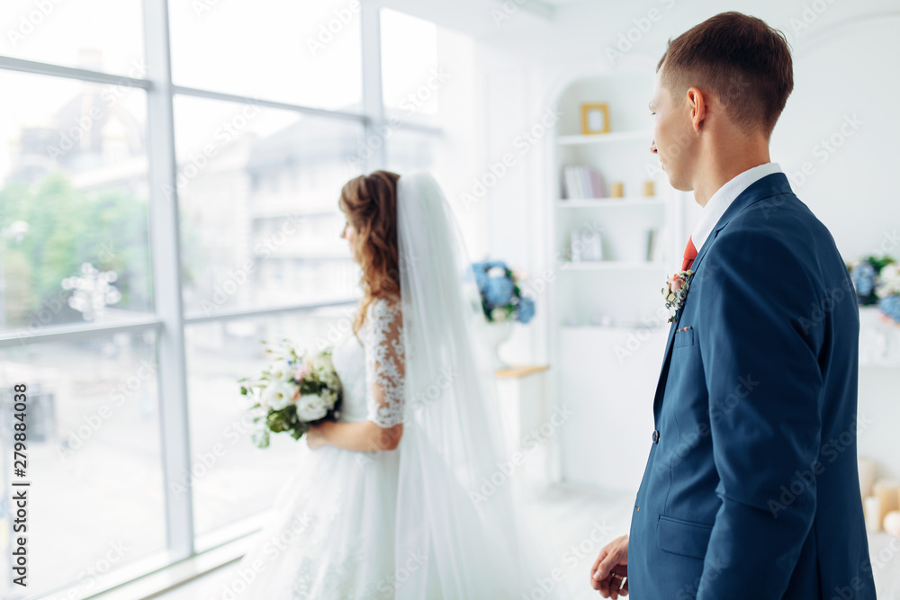 Beautiful bride in white dress and groom in suit, posing in white Studio interior, wedding