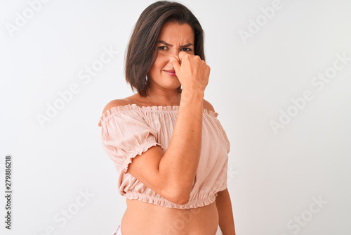 Young beautiful woman wearing casual t-shirt standing over isolated white background smelling something stinky and disgusting, intolerable smell, holding breath with fingers on nose. Bad smells 