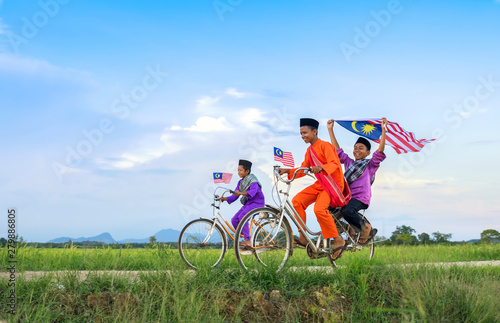 independence Day concept - Two happy young local boy riding old bicycle at paddy field holding a Malaysian flag photo