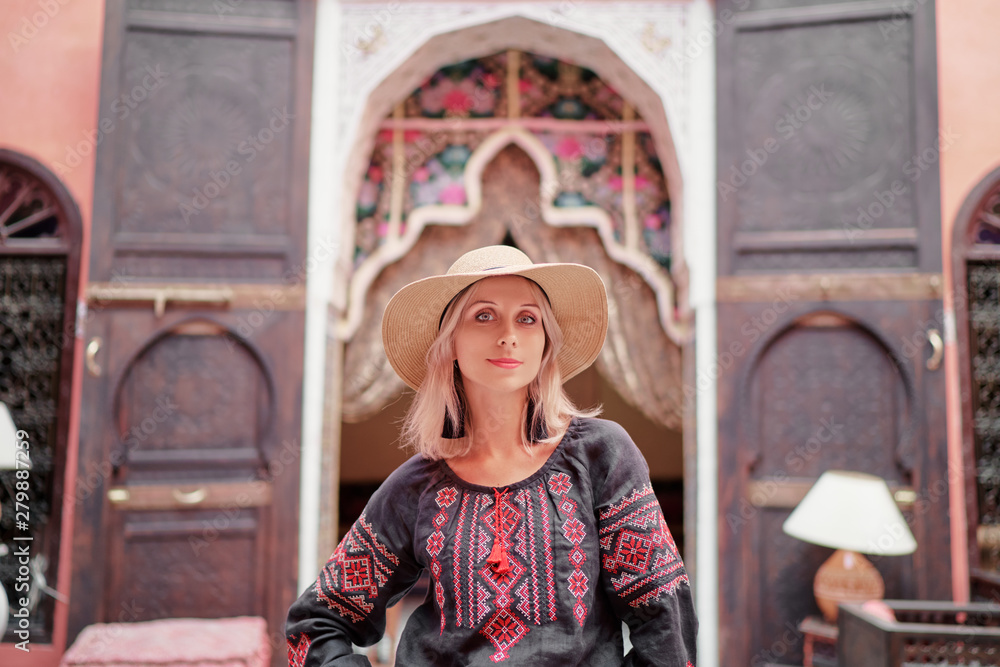 Traveling by Morocco. Happy young woman in hat relaxing in traditional riad interior in medina.