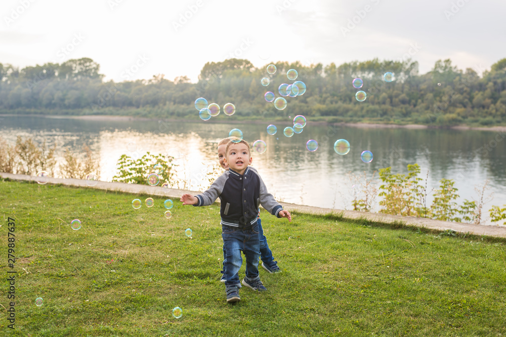 Children and childhood concept - Two brothers boys playing with colorful soap bubbles