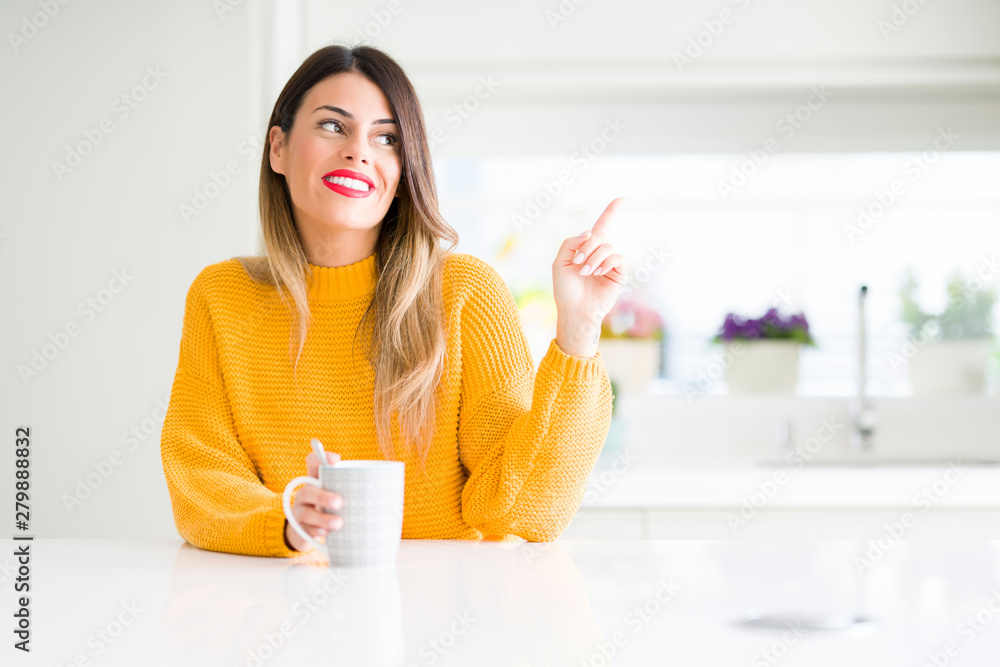 Young beautiful woman drinking a cup of coffee at home very happy pointing with hand and finger to the side Young beautiful woman drinking a cup of coffee at home very happy pointing with hand and finger to the side