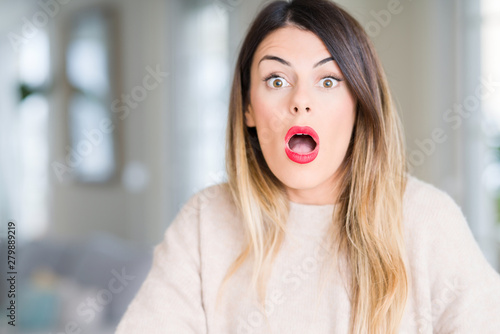 Young beautiful woman wearing winter sweater at home afraid and shocked with surprise expression, fear and excited face.