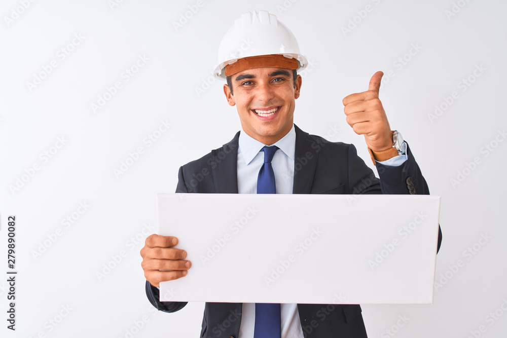 Young handsome architect man wearing helmet holding banner over isolated white background happy with big smile doing ok sign, thumb up with fingers, excellent sign Young handsome architect man wearing helmet holding banner over isolated white background happy with big smile doing ok sign, thumb up with fingers, excellent sign