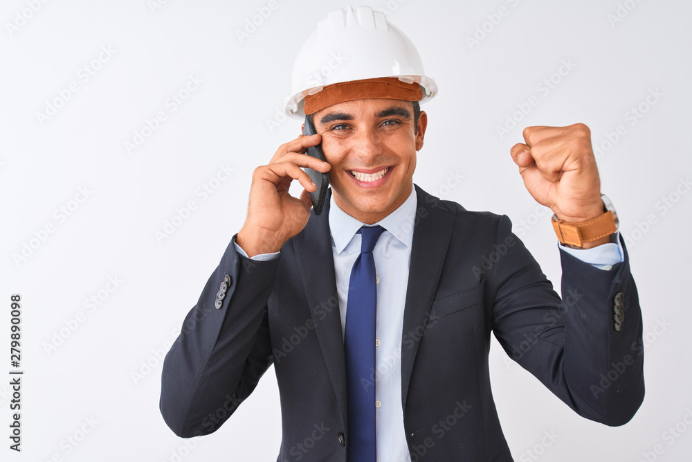 Young architect man wearing helmet talking on smartphone over isolated white background screaming proud and celebrating victory and success very excited, cheering emotion Young architect man wearing helmet talking on smartphone over isolated white background screaming proud and celebrating victory and success very excited, cheering emotion